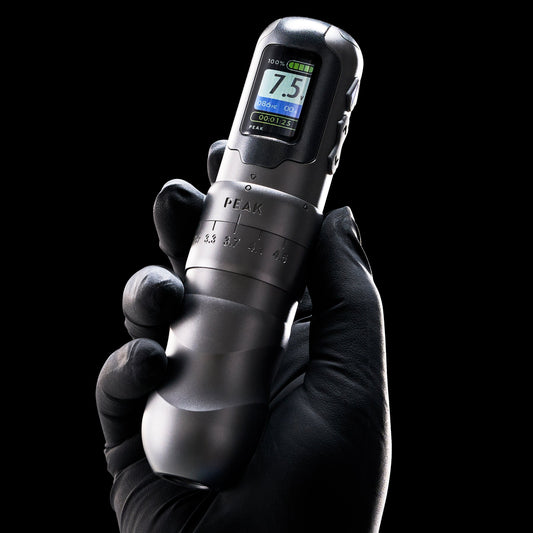 Gloved hand holding a Peak tattoo machine with adjustable stroke settings.
