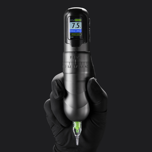 A sleek, gunmetal Peak wireless tattoo pen with a vibrant green cartridge held vertically in a gloved hand.