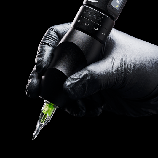 A gloved hand holding a black Peak Solice Pro tattoo machine with a needle cartridge against a black background.