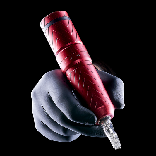 A gloved hand holding a red Peak tattoo pen machine with a chevron-patterned grip.